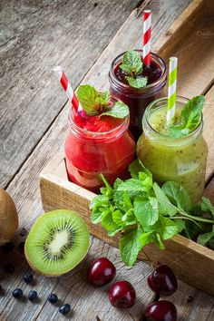 two mason jars filled with smoothies, cherries and kiwis on a wooden tray