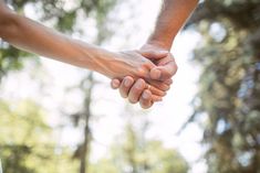 two people holding hands in front of trees