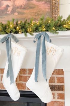 two stockings hanging from a mantel decorated with christmas lights and blue ribbon on the mantle