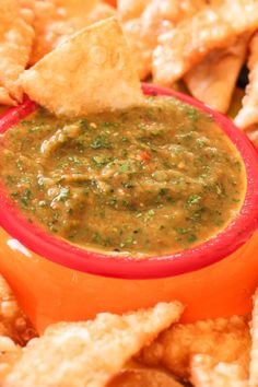 a red bowl filled with salsa surrounded by tortilla chips and dipping sauce on top