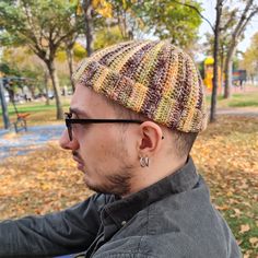 a man wearing glasses and a knitted hat sits on a bench in the park