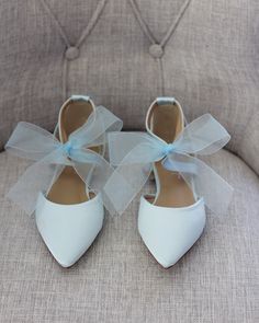 two pairs of white shoes with blue bows on the front and back, sitting on a couch