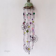 a metal bell hanging from the side of a wall with colorful beads and chains attached to it