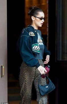 a woman in leopard print pants is walking out of a building with her handbag