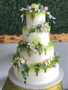 a three tiered wedding cake with flowers on top and greenery in the background