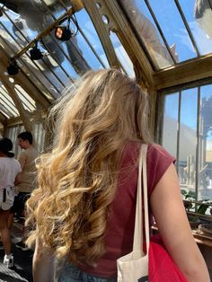 a woman with long blonde hair standing in front of a greenhouse looking out at the sky