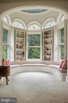 an arched window in the corner of a room with a bench and bookshelf