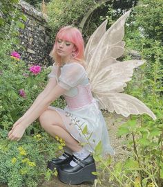 a woman dressed as tinkerbell crouching in the garden with flowers and plants around her