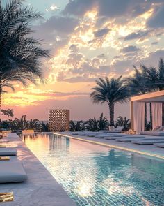 the sun is setting over an outdoor pool with lounge chairs and palm trees in front of it