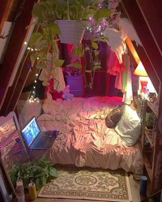 a bed room with a laptop on top of it and plants growing in the corner