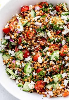 a salad with cucumber, tomatoes and feta cheese in a white bowl