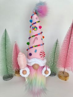 a pink and green gnome with candy canes in front of some christmas tree decorations