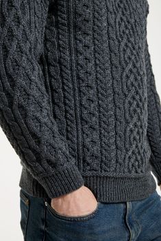 a close up of a person wearing a gray sweater and jeans with their hands in his pockets