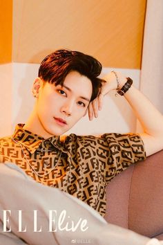 a young man sitting on top of a couch next to a white wall and wearing a brown shirt