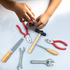 a child's hands holding various tools on top of a white table with scissors, pliers and wrenches