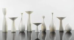 several white vases sitting on top of a black table next to eachother