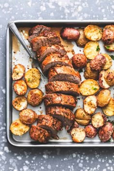 meat and potatoes on a baking sheet with a serving utensil next to it