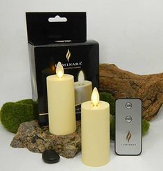 three lit candles sitting next to a remote control on a rock with moss growing around it