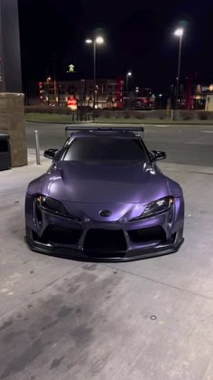 a purple sports car parked in front of a gas station at night with its hood up