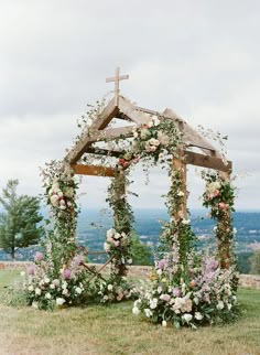 a wooden structure with flowers and greenery around it on the top of a hill