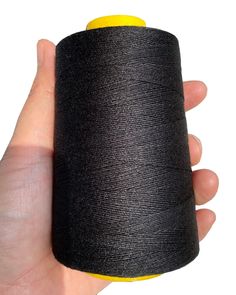 a hand holding a spool of black thread