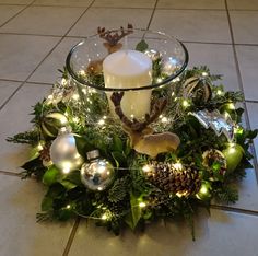 a glass bowl filled with christmas decorations on top of a tiled floor next to a candle