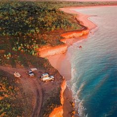 an aerial view of the beach with cars parked on it and cliffs in the background