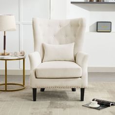 a white chair sitting next to a table with a lamp and other items on it