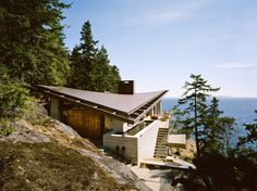 a house on top of a hill overlooking the ocean and trees with stairs leading up to it