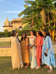 four women standing next to each other in front of a tree and building with palm trees