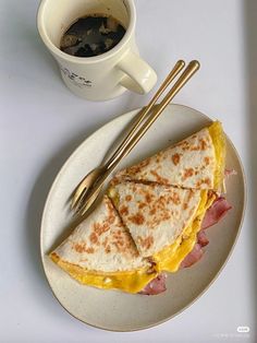 a plate with a sandwich and two chopsticks on it next to a cup of coffee