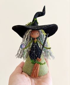 a hand holding a miniature witch doll with a broom