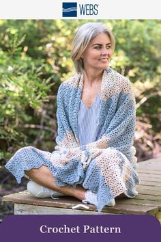 a woman sitting on top of a wooden bench wearing a blue and white knitted robe