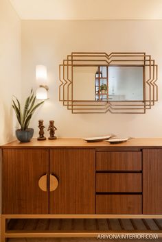 a large mirror on the wall above a wooden cabinet with two vases and a potted plant