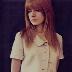 a woman with long red hair standing in front of a black background wearing a white suit