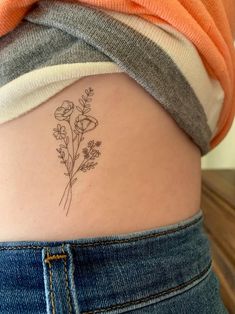 a woman's lower back tattoo with flowers on her left side ribcage