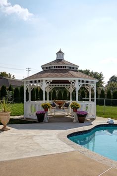 a gazebo sitting next to a swimming pool with potted plants on the side