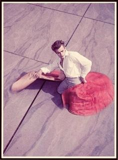 a man sitting on the ground next to a large red object with his legs spread out