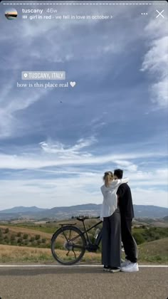 a man and woman standing next to each other on the side of a road with a bike