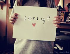 a girl holding up a sign that says sorry? with hearts drawn on it in front of her face