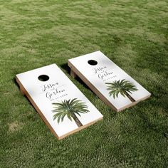 two cornhole boards with palm trees painted on them sitting in the middle of grass