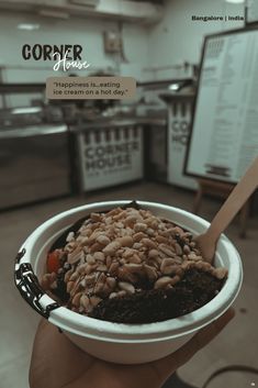 a person holding a bowl filled with food in front of a sign that reads corner house