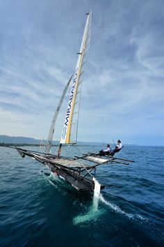 a sailboat with two people on it in the water near shore line and blue sky