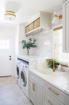 a washer and dryer in a white kitchen with marble counter tops, gold accents