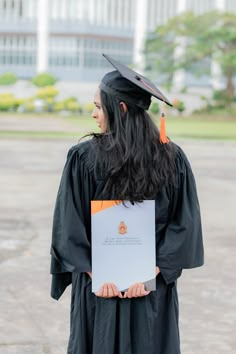 a woman with long black hair wearing a graduation gown and holding a white piece of paper