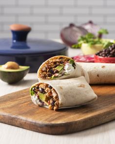 two burritos sitting on top of a wooden cutting board next to an avocado