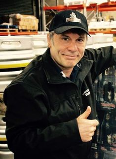 a man in a black jacket and hat holding a snowboard with his thumb up