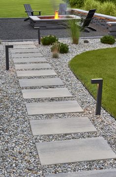 a fire pit sitting in the middle of a garden next to a gravel path and lawn chairs