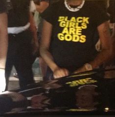 two people standing next to each other in front of a car with black girls are gods t - shirt on