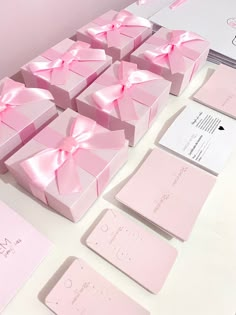 many pink boxes with bows on them are sitting on a table next to cards and envelopes